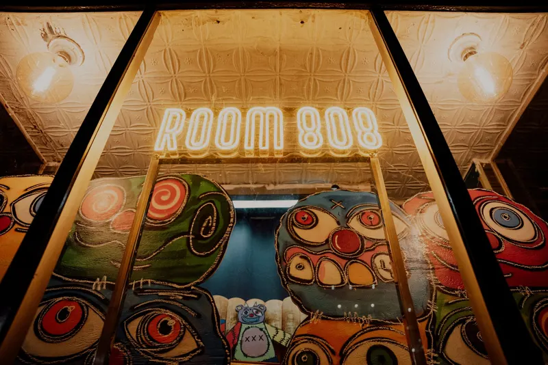 The gold neon Room 808 sign over the painted window faces