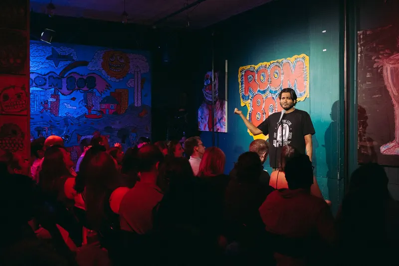 A comic on stage, the logo wall and a packed room