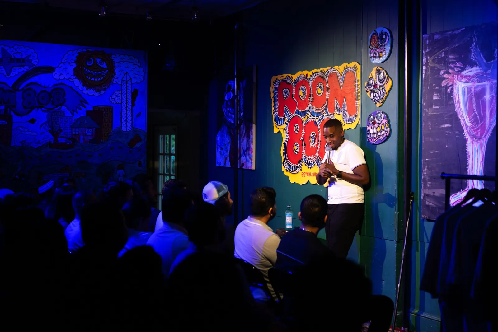 A comic on the Room 808 stage under the mural, crowd in front