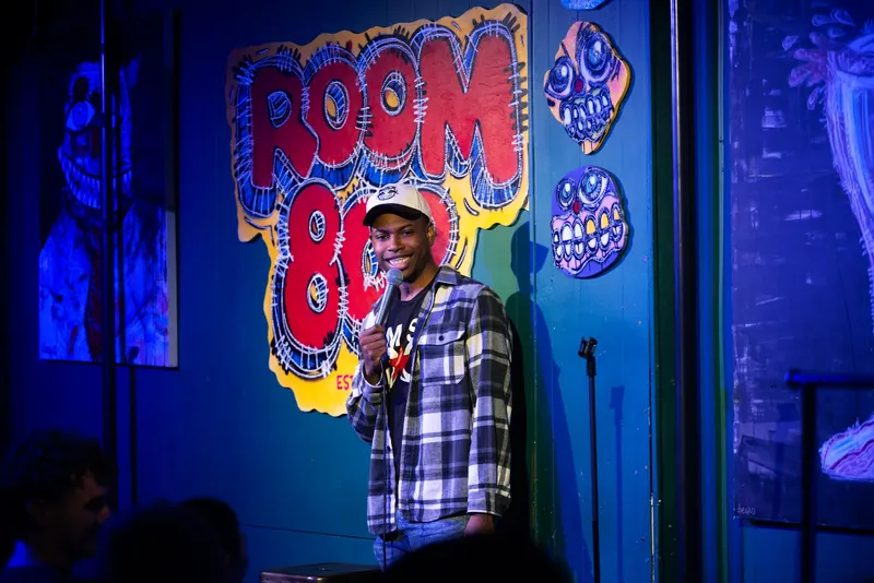 A comic on stage in front of the Room 808 logo wall